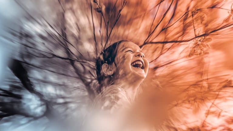 Double exposure of a child laughing joyfully and blurred golden leaves and branches: happiness and nature concept.