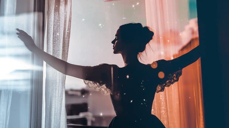 Double exposure of a silhouette of a woman with arms outstretched at a softly lit window