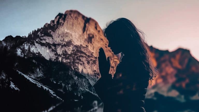 Double exposure of a silhouette of a woman with hands in prayer position and a mountain illuminated by sunset: serenity and reflection concept.