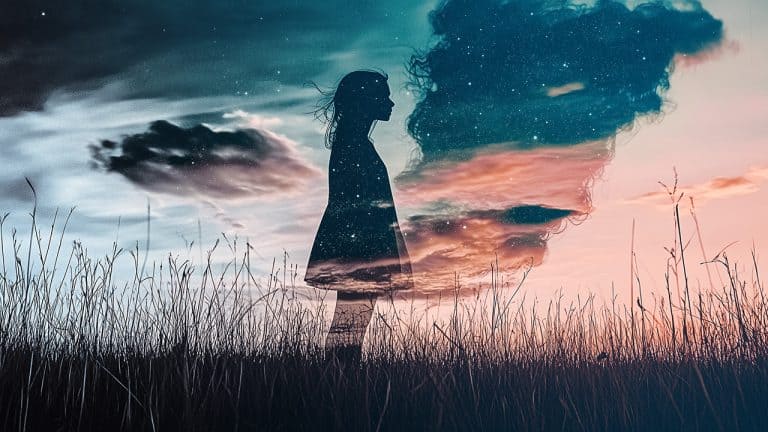 Double exposure of a silhouette of a woman standing in a field and a starry night sky with clouds: dreamlike and contemplative concept.