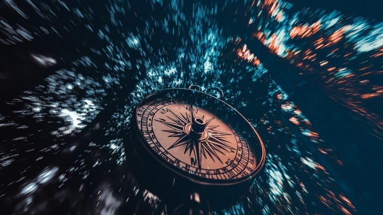 Double exposure of a close-up compass and a blurred view of tall trees in a forest: navigation and exploration concept.