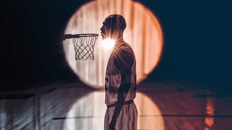Double exposure of a silhouette of a basketball player in profile and a bright sun setting behind a basketball hoop: determination and focus concept.