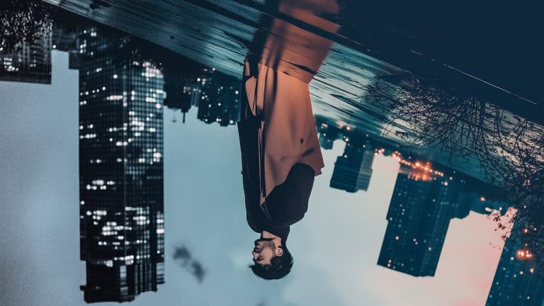 Double exposure of a man standing thoughtfully with his reflection merging into a city skyline at dusk: introspection and urban solitude concept.