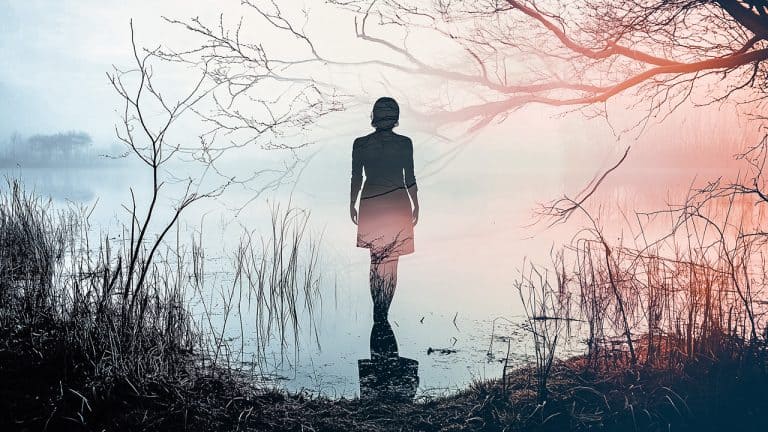 Double exposure of a silhouette of a woman standing and facing a misty lake