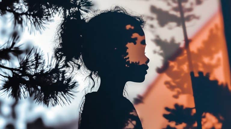 Double exposure of a silhouette of a child with curly hair and trees with branches against a warm