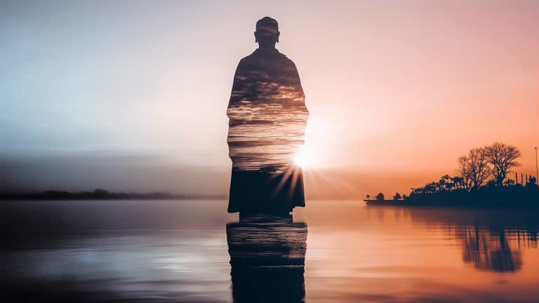 Double exposure of a silhouette of a person standing and a vibrant sunset over a calm lake with trees: tranquility and reflection concept.